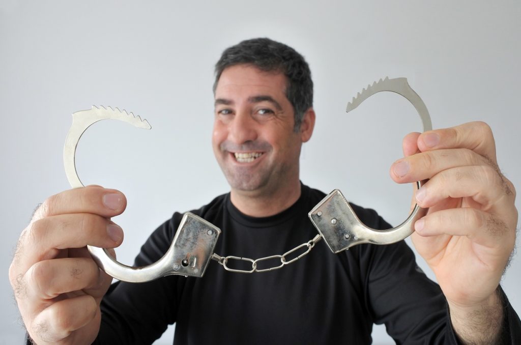 A happy free man (age 40) holds unlocked handcuffs in front of the camera. 