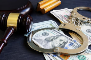 A gavel, money, and handcuffs all sit on a table 